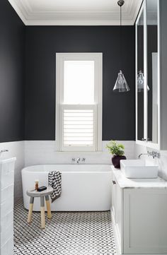 a white bath tub sitting under a bathroom window next to a sink and a mirror