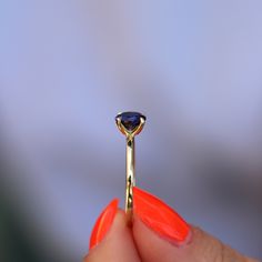 a woman's hand holding an orange manicured nail with a ring on it