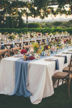 an outdoor table set up with blue and white linens, flowers and candles on it