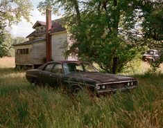 an old car is parked in the tall grass near a house that has been abandoned