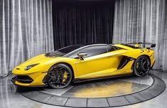 a yellow sports car sitting on top of a circular floor in front of curtains and drapes