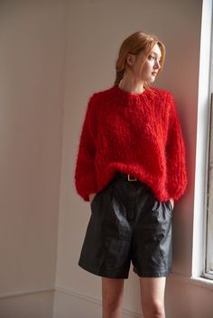 a woman standing in front of a window wearing black shorts and a red fuzzy sweater