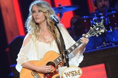 a woman holding an acoustic guitar while standing in front of a microphone and playing the guitar