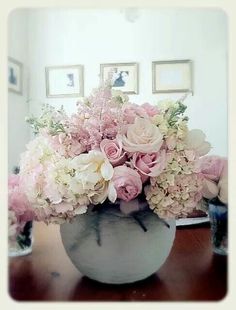 a vase filled with pink and white flowers sitting on top of a wooden table next to framed pictures