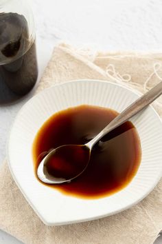 a white plate topped with sauce next to a jar of liquid and a spoon on top of a napkin