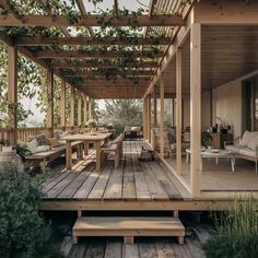 a wooden deck with benches and tables under a pergolated roof, surrounded by greenery