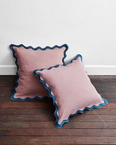 two pink pillows with scalloped edges sit on a wooden floor next to a white wall