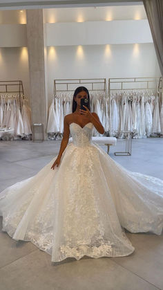 a woman in a wedding dress taking a selfie with her cell phone while standing next to a rack of dresses