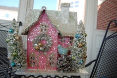 a small pink house with trees and snow on the roof in front of a window