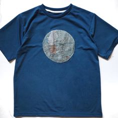 a blue t - shirt with a circular design on the front and back, sitting on a white surface