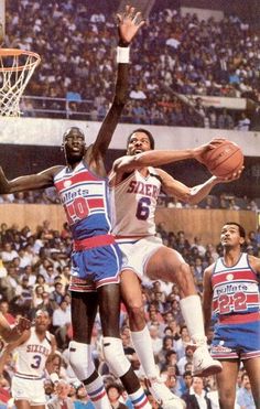 the basketball players are trying to block the ball from going into the hoop in front of the crowd