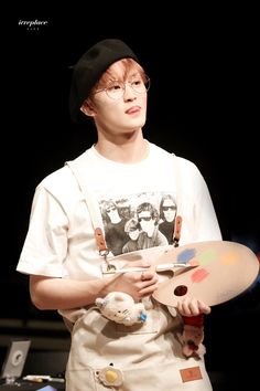 a boy with glasses and an apron holding a paintbrush in one hand while standing on stage