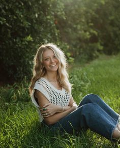 a woman sitting in the grass with her arms crossed and looking at the camera smiling