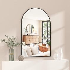 a living room with a white couch and mirror on the fireplace mantel next to a potted plant