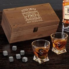 two whiskey glasses next to an empty wooden box and ice cubes