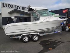 a white boat is parked in front of a luxury boat store with a trailer attached to it