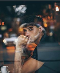 a man sitting at a table with his hand on his mouth and looking out the window