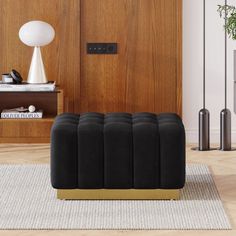 a black ottoman sitting on top of a wooden floor next to a lamp and bookshelf