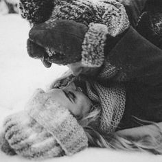 a black and white photo of a woman laying in the snow with a teddy bear on her head