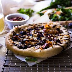 a pizza sitting on top of a cooling rack next to a glass of wine and other food