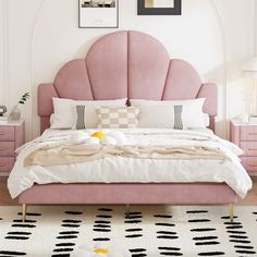 a bed with pink headboard and pillows in a white walled room next to two pictures on the wall