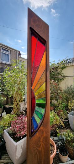 a colorful stained glass window sitting on top of a wooden stand next to potted plants