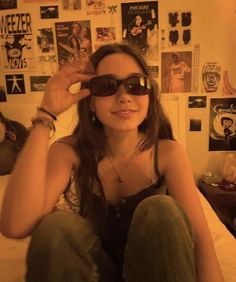 a woman sitting on top of a bed wearing sunglasses and holding her hand up to her eye