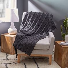 a chair with a blanket on top of it in front of a table and lamp