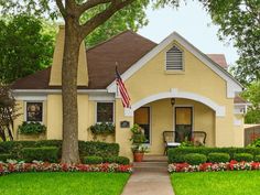 a yellow house with an american flag on the front door and landscaping in front of it