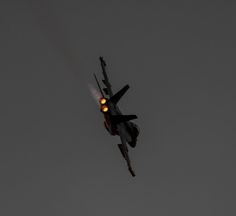 a fighter jet flying through the air with it's landing gear down and its lights on