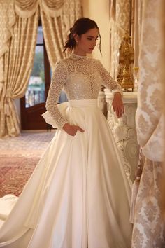 a woman standing in front of a mirror wearing a wedding dress with long sleeves and bow at the waist