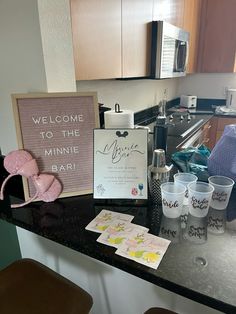 a kitchen counter topped with lots of cups and magnets next to a sign that says welcome to the mininie bar