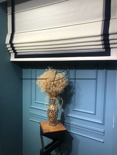 a vase filled with dried flowers sitting on top of a wooden stool next to a blue wall