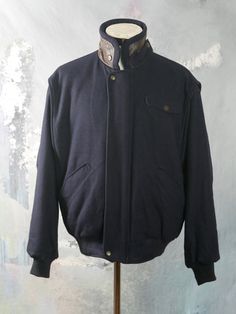 "This 1990s vintage jacket is a dark navy blue color and has a rounded wing collar that shows the brown genuine leather underside when you wear the collar turned up. The warm jacket zips closed in front and has two snap buttons to further secure it. When worn with the \"lining\" showing, you have a completely different and colorful look and feel (cotton fabric in green, tan, and fuchsia, with purple satin acetate sleeves). Note that if you want to wear the colorful side, you zip the jacket close Vintage Blue Outerwear With Button Closure, Vintage Blue V-neck Outerwear, Vintage Faded Pre-washed Outerwear, Vintage Wool Double-breasted Outerwear, Vintage Blue Pre-washed Outerwear, Wing Collar, Long Overcoat, Brown Tweed, Tweed Coat