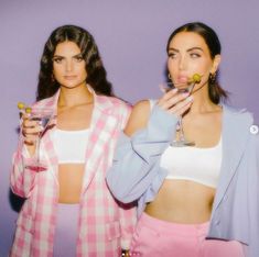 two beautiful women standing next to each other holding drinks in front of their faces and looking at the camera