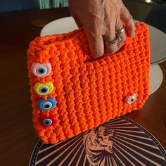 an orange crocheted purse with eyeballs on the front and sides, being held by a woman's hand