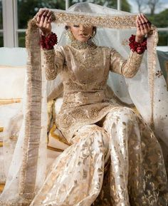 a woman sitting on top of a bed wearing a white and gold dress with red beads