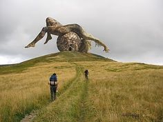 two people walking up a hill with a giant object in the sky above them,