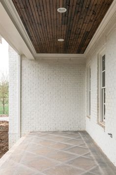 an empty porch with white brick walls and wood ceilinging on the side of it