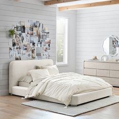 a white bed sitting in a bedroom next to a dresser under a window with pictures on it