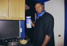 a man standing in front of a stove holding up a box of cereal and looking at the camera