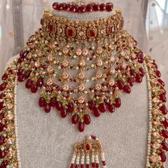 an elaborate necklace and earring set with red stones on display in front of a mannequin