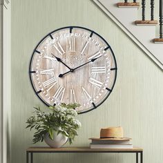 a clock that is on the wall next to a table with flowers in front of it