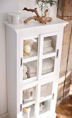 a white cabinet with glass doors and shelves filled with folded towels on top of it