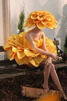 a woman sitting on top of a wooden bench wearing a dress made out of flowers