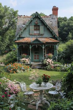 a green house surrounded by flowers and greenery with a table in the foreground