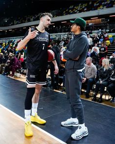 two men standing on top of a basketball court next to each other in front of an audience