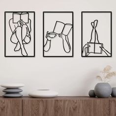 three black and white paintings hanging on the wall next to a vase with flowers in it