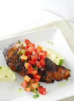 a white plate topped with meat covered in fruit and veggies next to a slice of lime