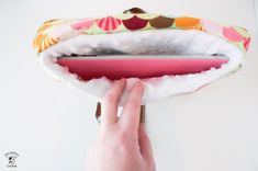 a hand is holding an open laptop computer case in front of a white wall with a pink handle